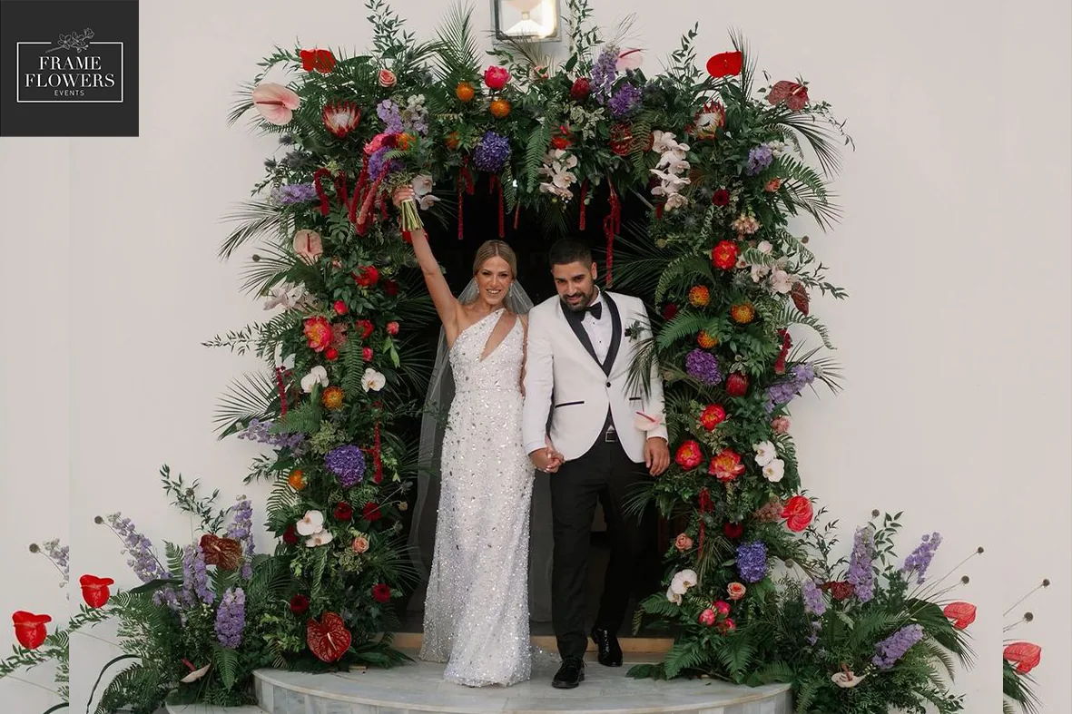 Bride and groom under a lush floral arch at a wedding in Cyprus